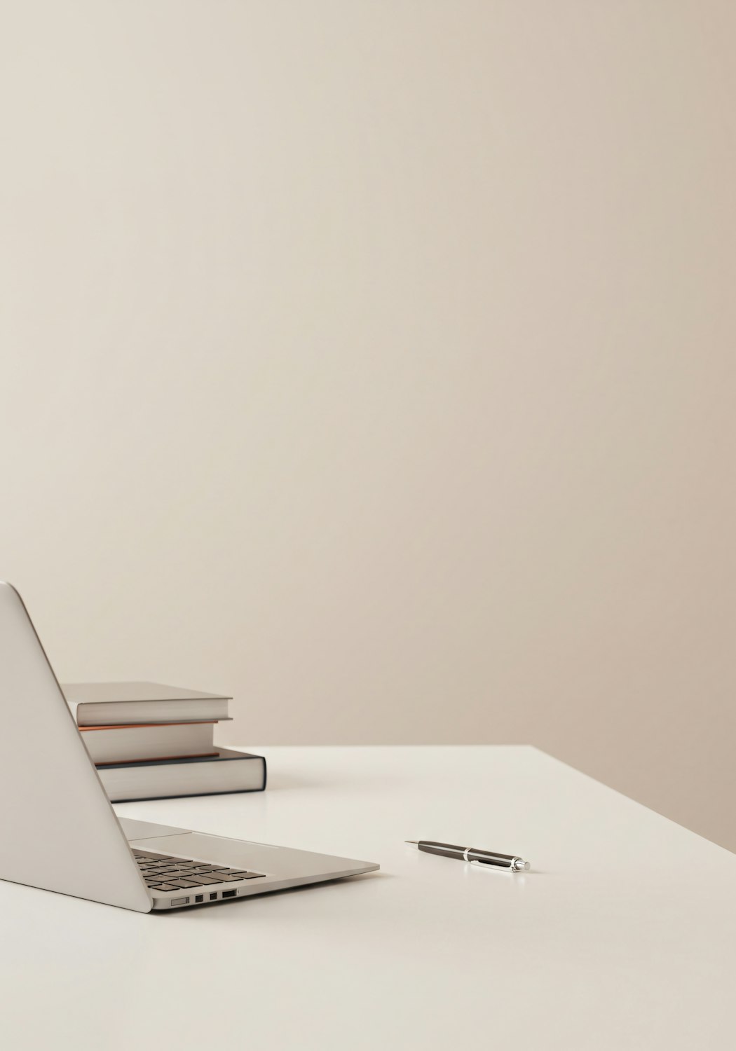 A minimal studio desk with a laptop, notebooks, and a pen